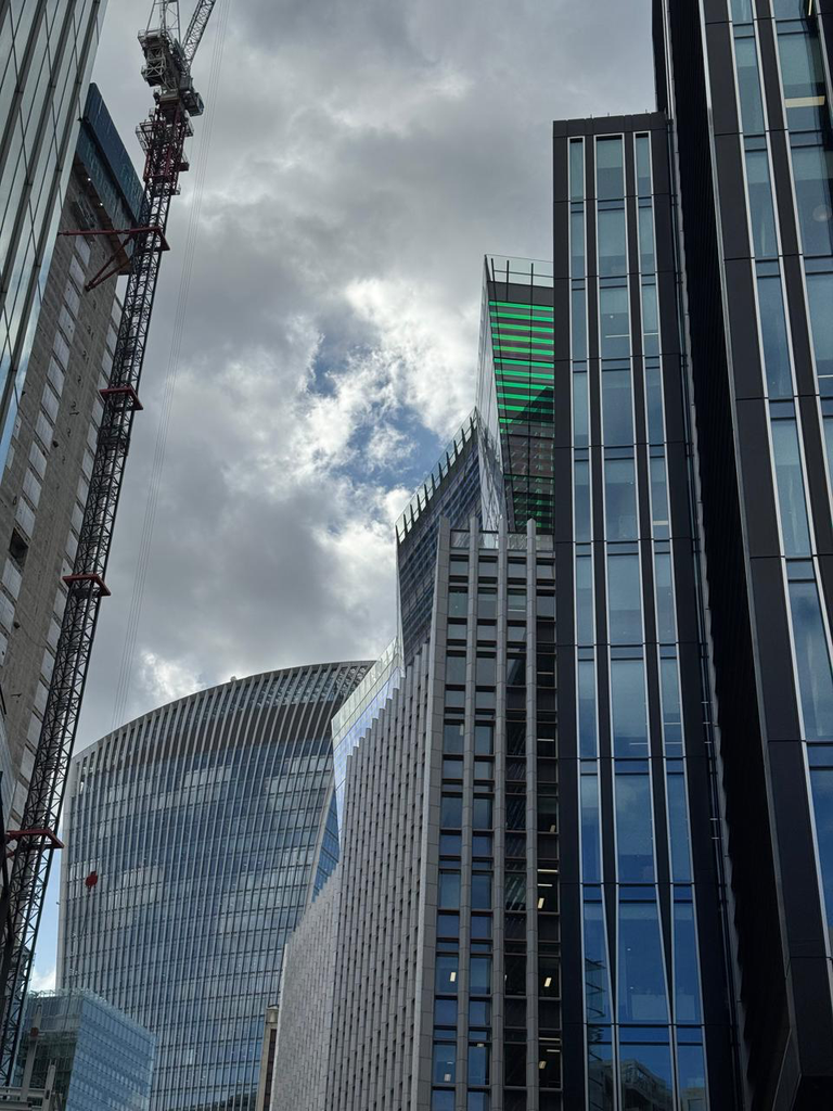 Low-angle view of modern glass skyscrapers and a tall construction crane against a cloudy sky