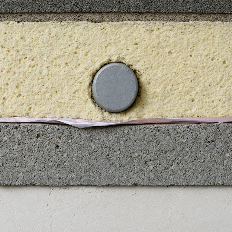 Wall cross-section exposing insulation layers with an embedded battery cell, illustrating energy storage integration risks in building assemblies.