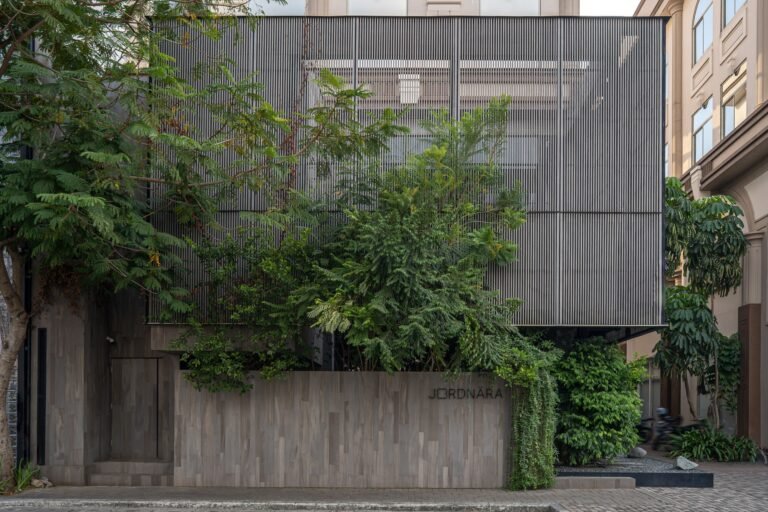 Exterior view of Phomi Cafe showing vertical metal louvers and lush greenery screening the main building facade.