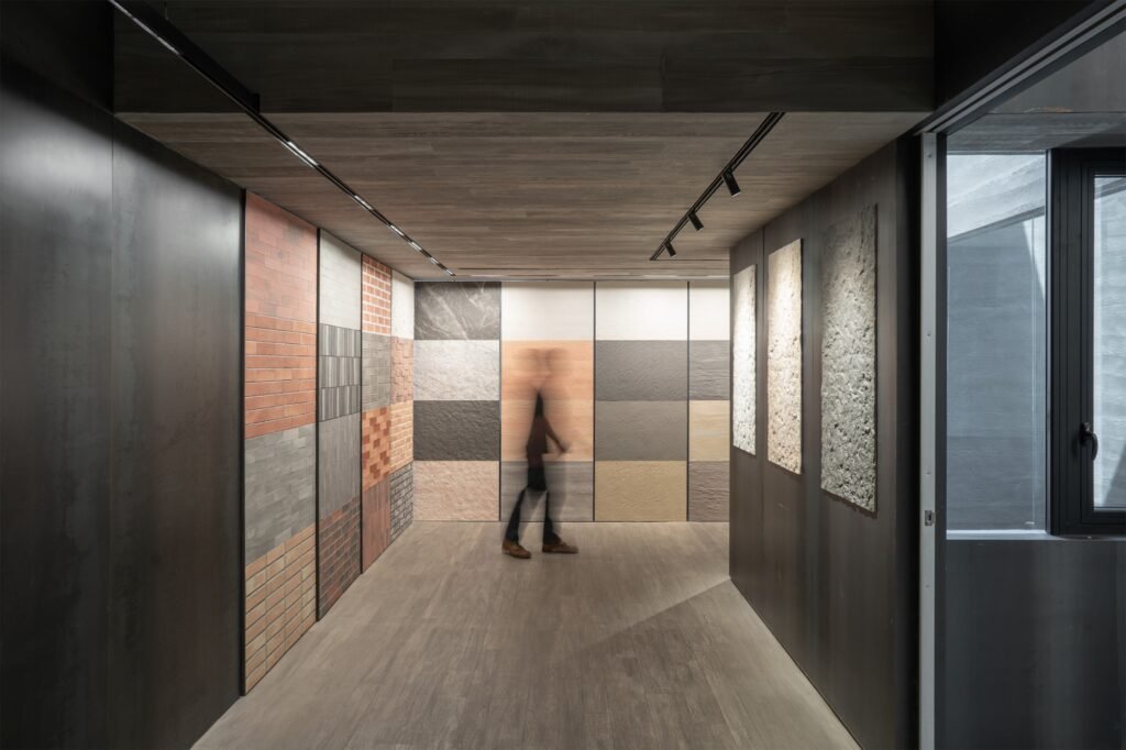 Minimalist showroom hallway displaying Phomi Econic Clay cladding material samples on dark walls under track lighting.