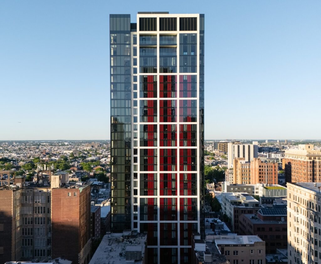 Straight-on architectural facade view of 210 South 12th residential tower in Philadelphia featuring a white grid frame and red corrugated shadow box panels.