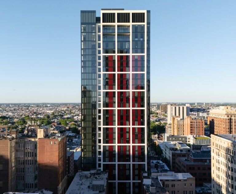 Straight-on architectural facade view of 210 South 12th residential tower in Philadelphia featuring a white grid frame and red corrugated shadow box panels.