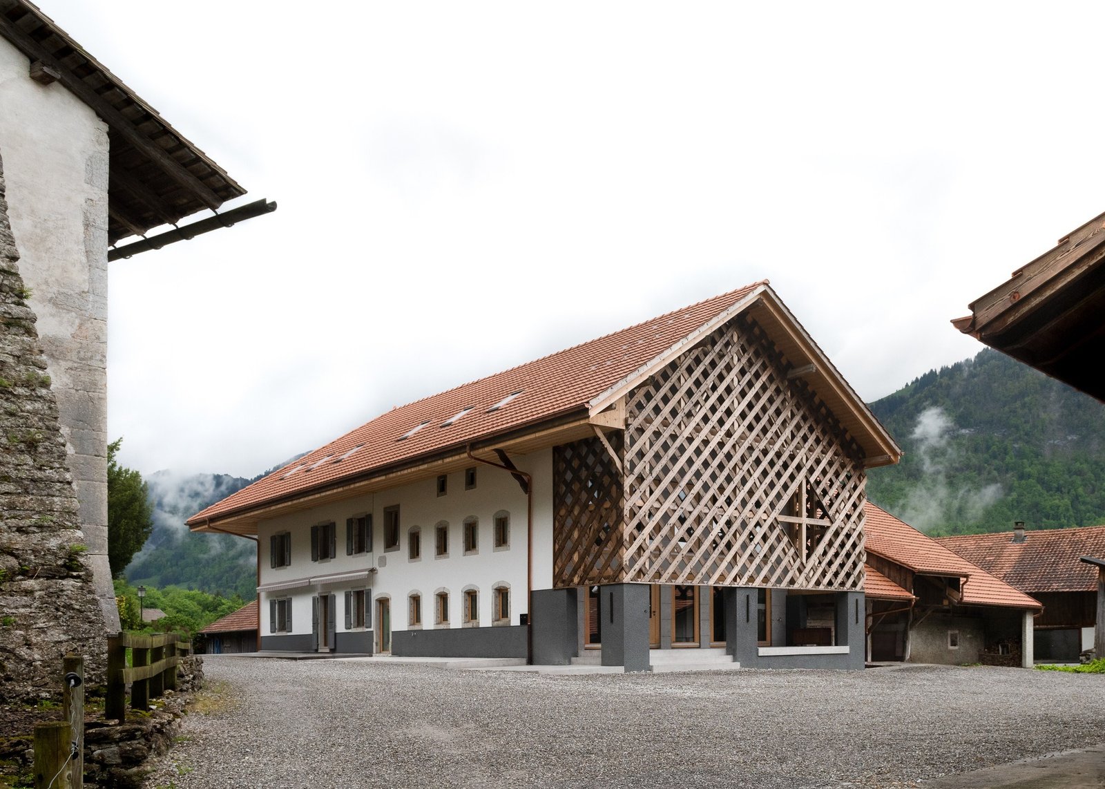 Exterior view of the renovated 18th-century Grandvillard farmhouse featuring a traditional tiled roof, white masonry facade, and an intricate wooden lattice screen on the converted agricultural wing.