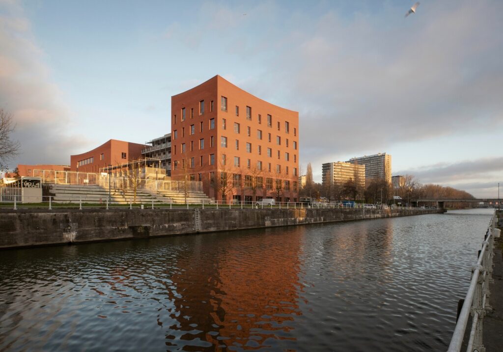 Exterior view of Campus Deleers showing red brick buildings along the Brussels canal with public promenade.