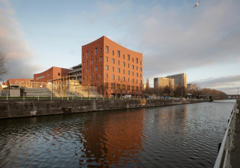 Exterior view of Campus Deleers showing red brick buildings along the Brussels canal with public promenade.