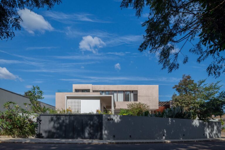 Front facade of Casa Noor featuring textured plaster finish, cobog&oacute; screen, and surrounding foliage under a clear blue sky.