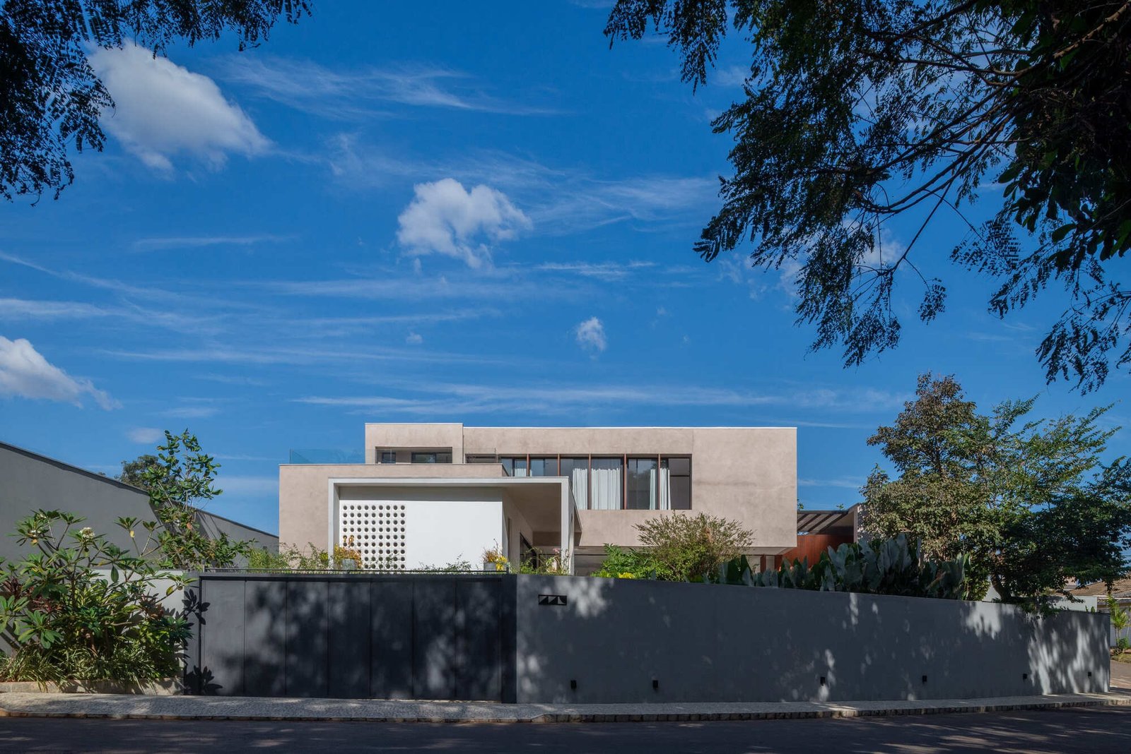 Front facade of Casa Noor featuring textured plaster finish, cobogó screen, and surrounding foliage under a clear blue sky.