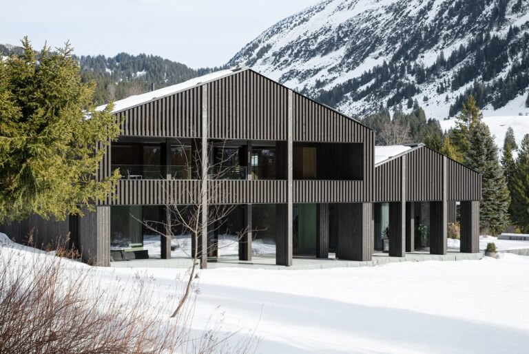 South elevation of the multi-generational Alpamyr house featuring dark stained spruce cladding and covered balconies in a snowy mountain landscape.