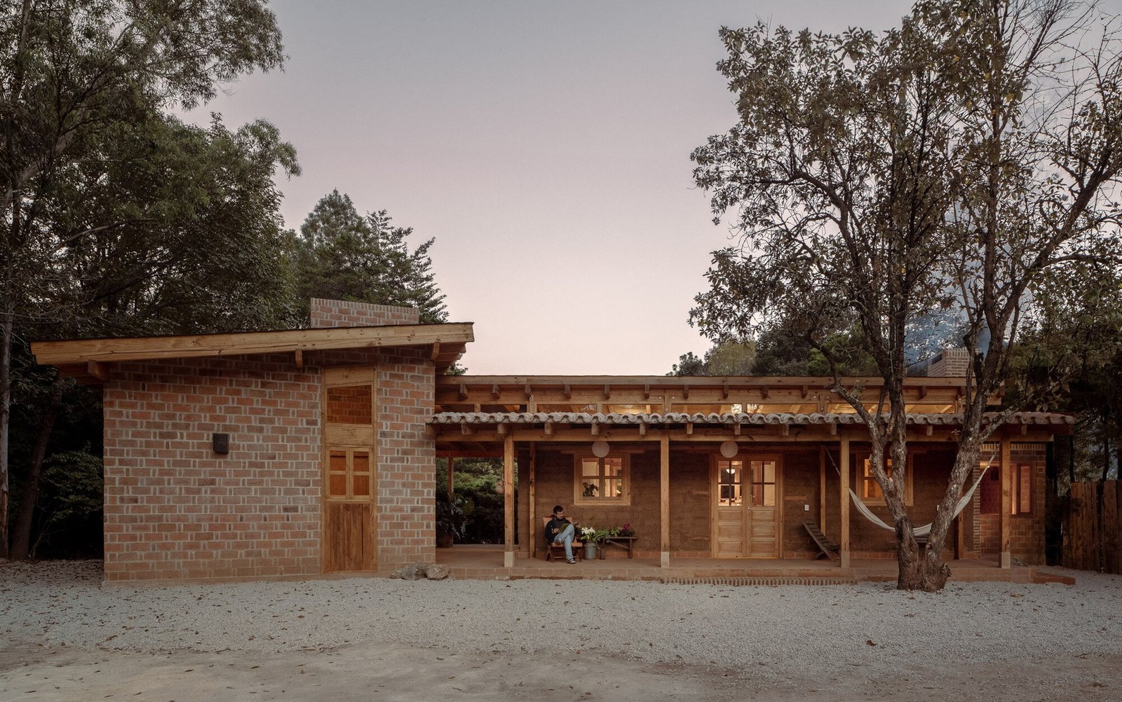 Wide front elevation of Casa Esteli at twilight showing the old adobe block structure flanked by new red brick extensions under a timber roof overhang.