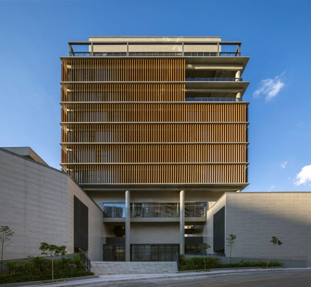 Front view of the Colégio Bernoulli administrative tower featuring vertical sunshades and raw concrete pillars at the entrance.