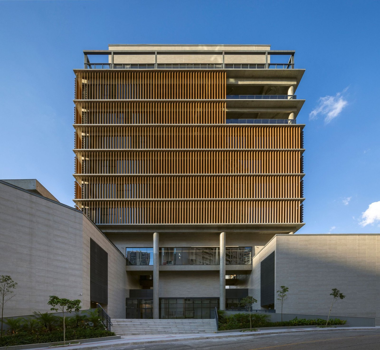 Front view of the Colégio Bernoulli administrative tower featuring vertical sunshades and raw concrete pillars at the entrance.
