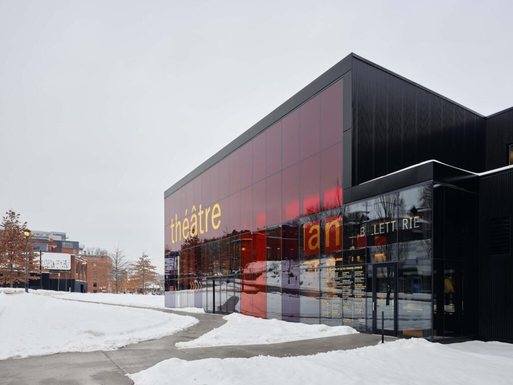 Exterior front view of Le Grand-Espace in Sherbrooke featuring a translucent red and dark glass curtain wall set in a snowy urban landscape.