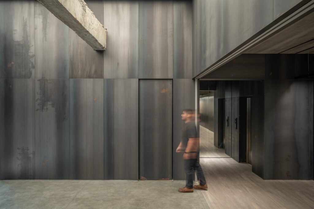 Double-height interior hallway with dark textured walls, exposed concrete beams, and dim lighting.
