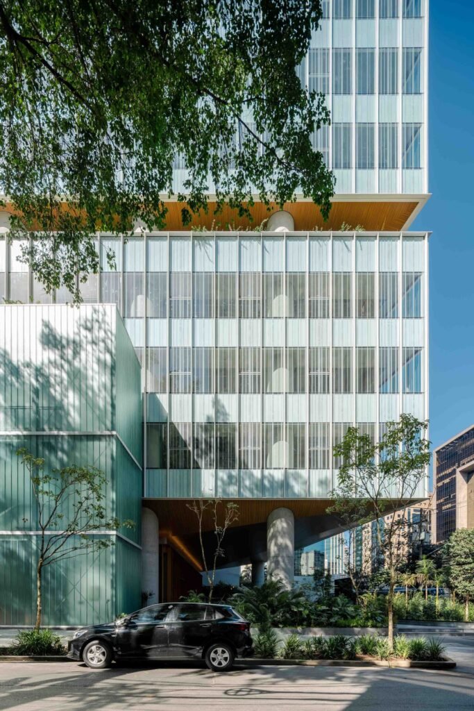 Street-level view of Jer&ocirc;nimo Faria Lima featuring massive exposed concrete columns supporting a cantilevered upper block with silk-screen printed glass patterns.