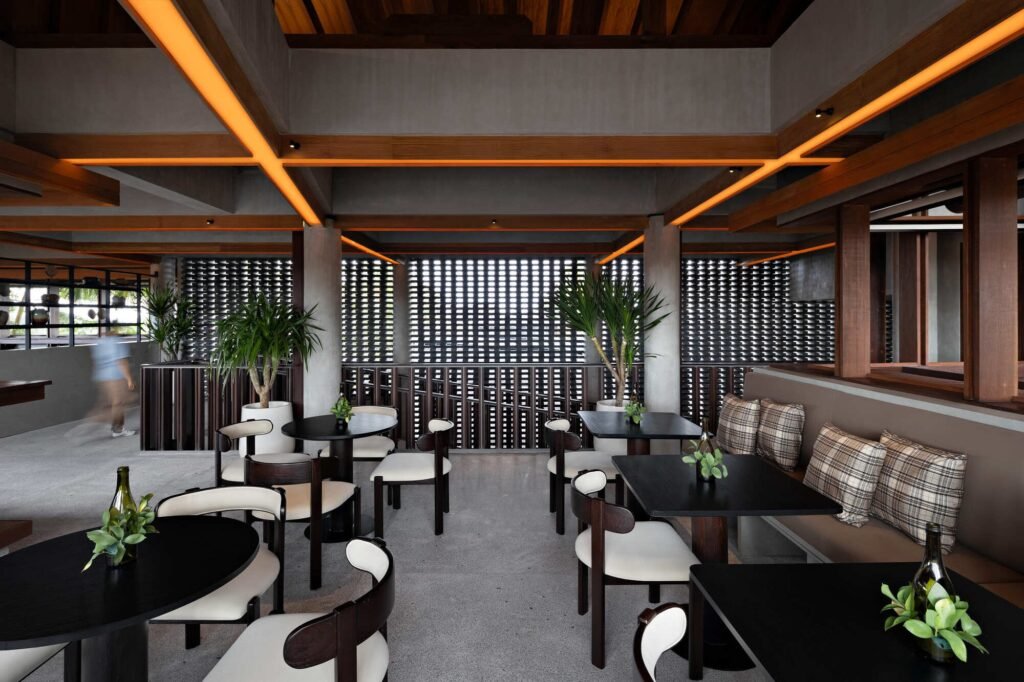 Open-plan indoor dining area at Kemilu Ubud with wooden furniture, perforated brick screen wall, and warm ceiling grid lighting.