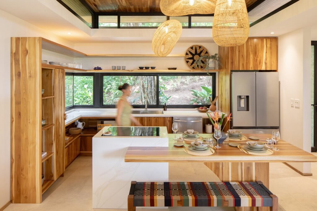 Modern open-plan kitchen and dining interior featuring natural teak wood cabinetry and clerestory window lighting.