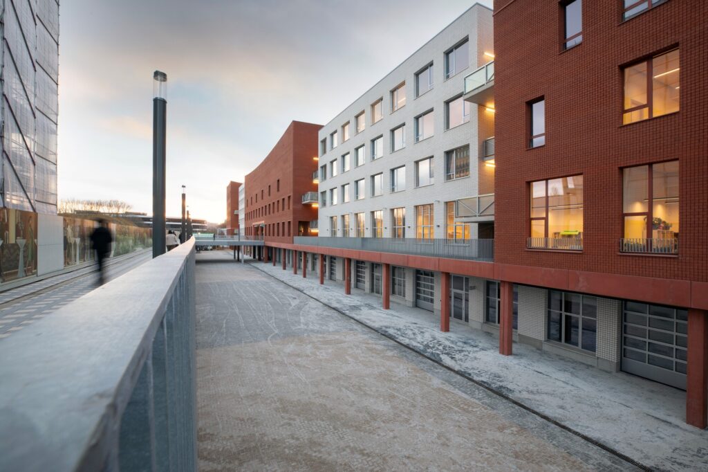 Lower-level access street with red columns beneath mixed-use brick and tiled buildings at Campus Deleers.