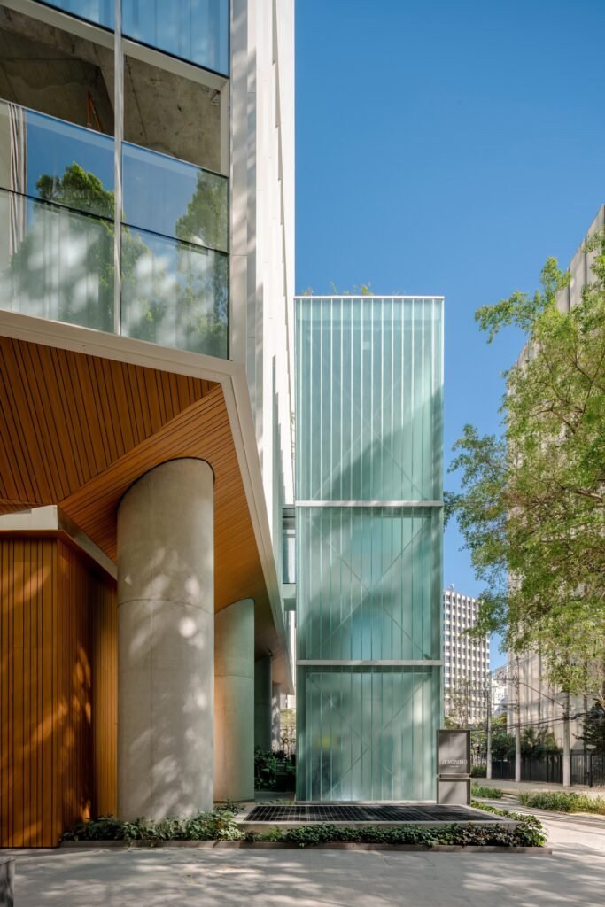 Angled low-angle view of the building approach featuring wood-clad soffit ceiling, concrete structural column, and translucent glass circulation shaft.