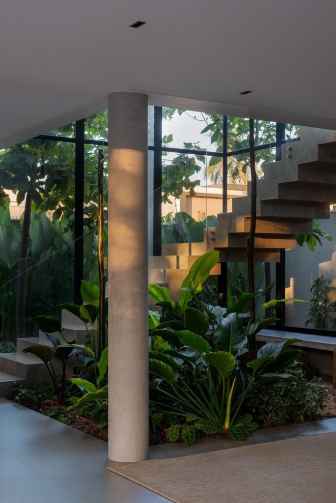 Indoor tropical garden positioned underneath a floating concrete staircase inside Casa Noor.