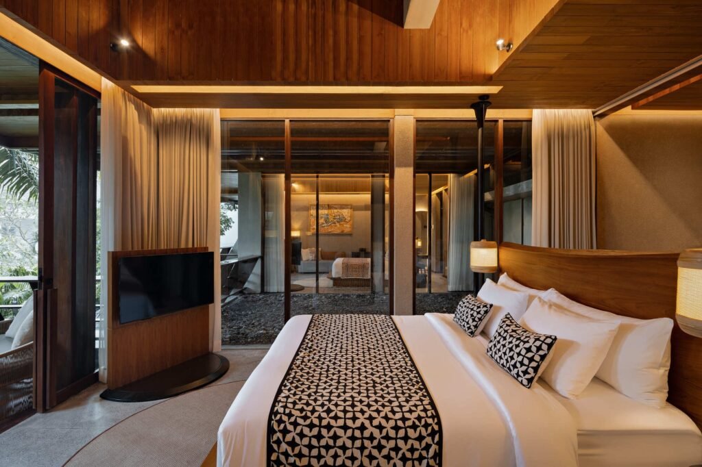 Luxury guest room interior at Kemilu Ubud with natural timber ceiling, patterned bed runner, and floor-to-ceiling glass doors facing the landscape.