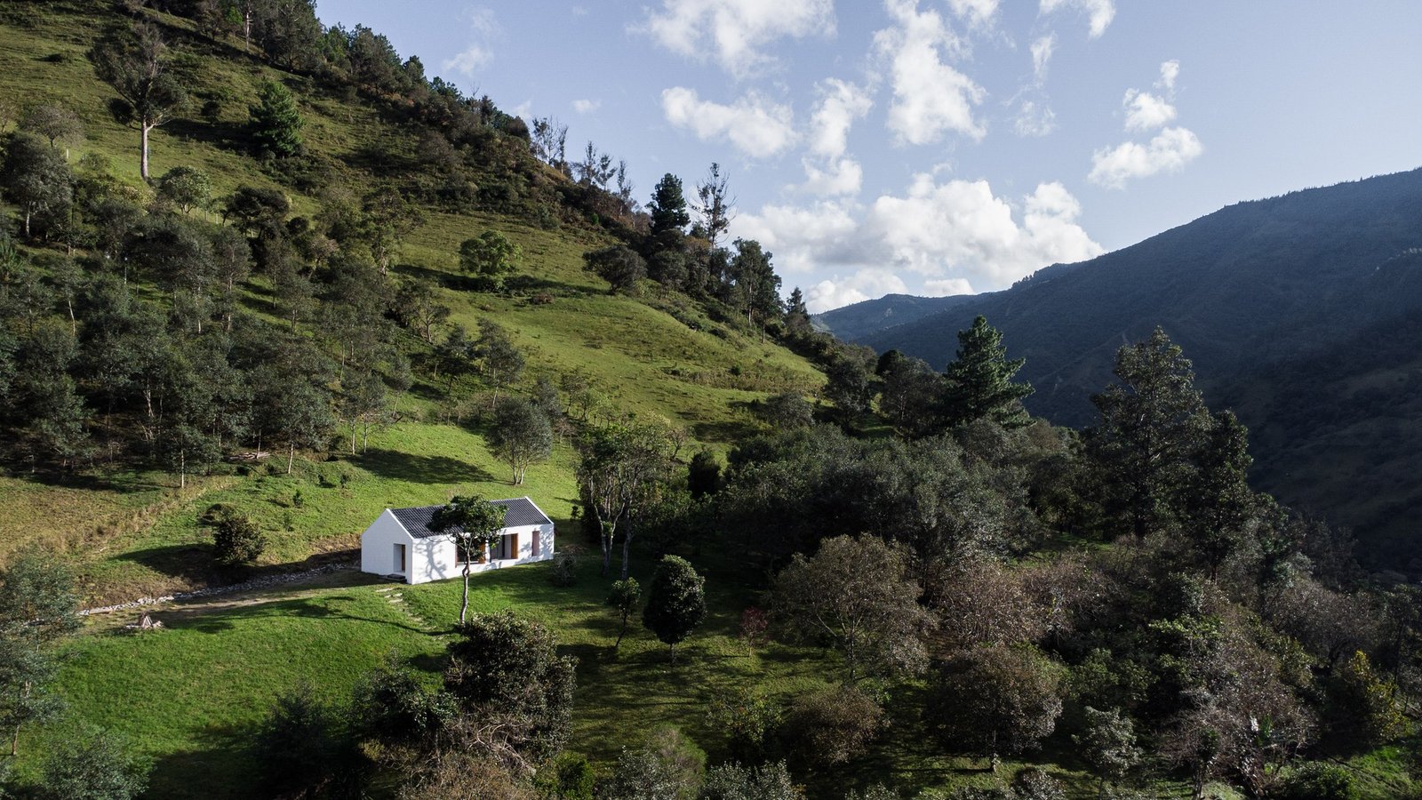 Aerial landscape view of Casa Florinda resting on a grassy hill surrounded by lush green trees and mountain valleys in Ecuador.