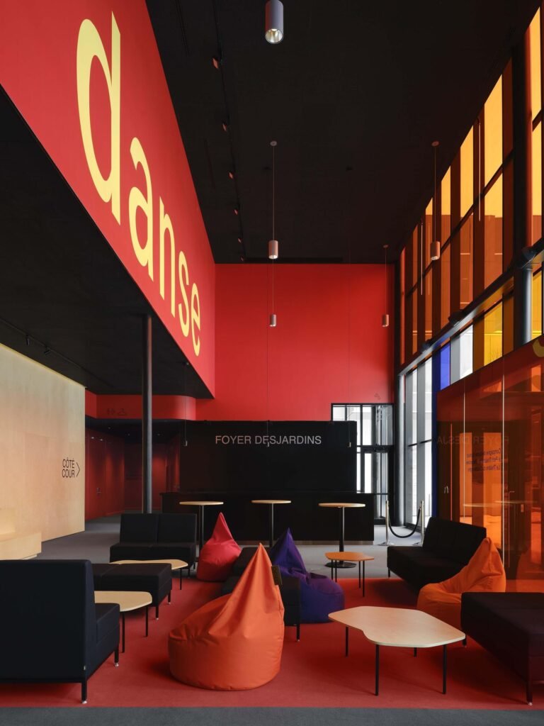 Interior foyer of Le Grand-Espace with bold red wall graphics displaying 'Danse', casual beanbag seating, and the Foyer Desjardins desk.