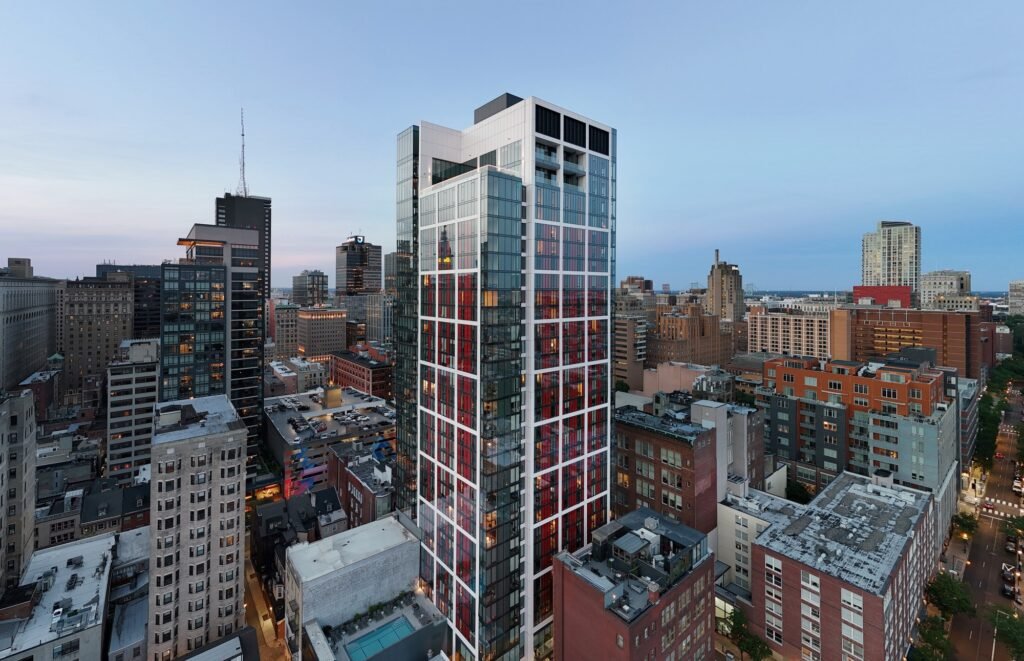 High aerial view at dusk showing 210 South 12th tower illuminated within the dense Center City Philadelphia neighborhood.