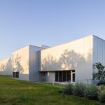 Metallic corrugated metal facade of the Crux South building framed by green lawn and trees.