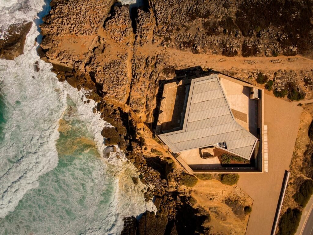 Top-down aerial drone view of Cresmina Fort positioned on a rugged rocky coastal cliff in Cascais with crashing sea waves.