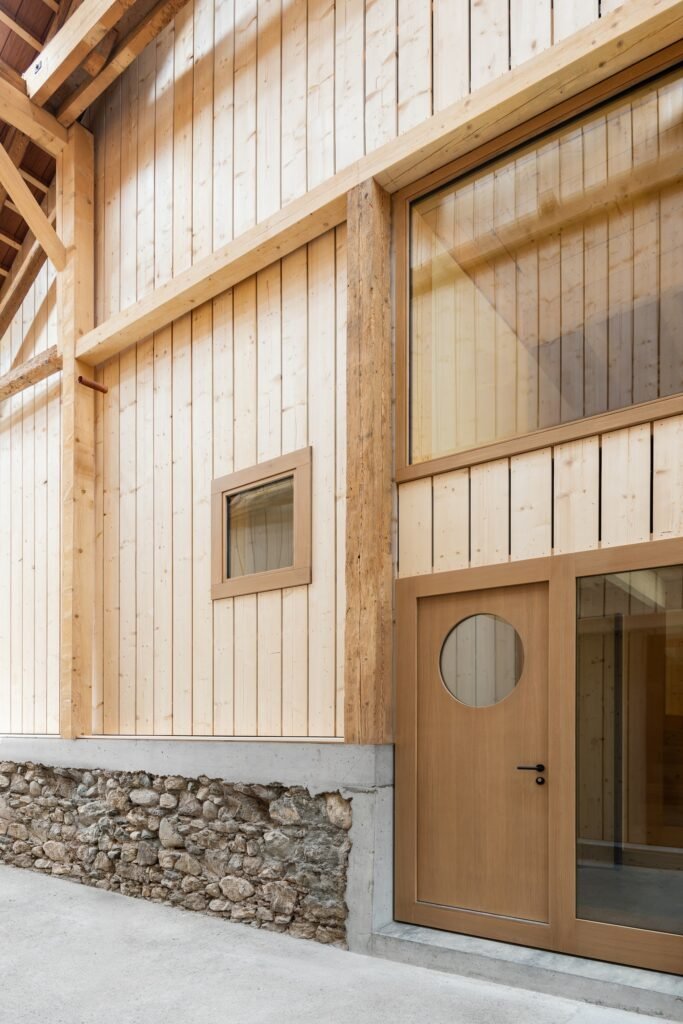 Architectural detail of light pine wall paneling set over an original rough stone foundation with modern timber door framing and circular porthole window.