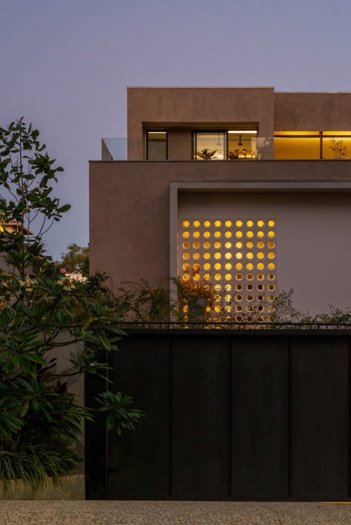 Twilight view of Casa Noor highlighting warm interior light shining through a circular cobog&oacute; block wall.