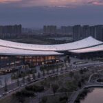 Exterior twilight view of the Xi'an Public Library on the Ba River bank showing its sweeping curved roofline and illuminated glass facade.