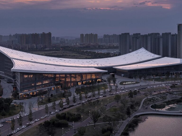 Exterior twilight view of the Xi'an Public Library on the Ba River bank showing its sweeping curved roofline and illuminated glass facade.