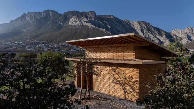 Exterior wide shot of La Grieta Pavilion featuring stacked wooden block walls and an angled roof, set against a dramatic mountain backdrop.