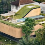 Aerial view of Split Mass Residence featuring a sloped green roof, swimming pool, wooden pergola, and woven synthetic rattan facade.