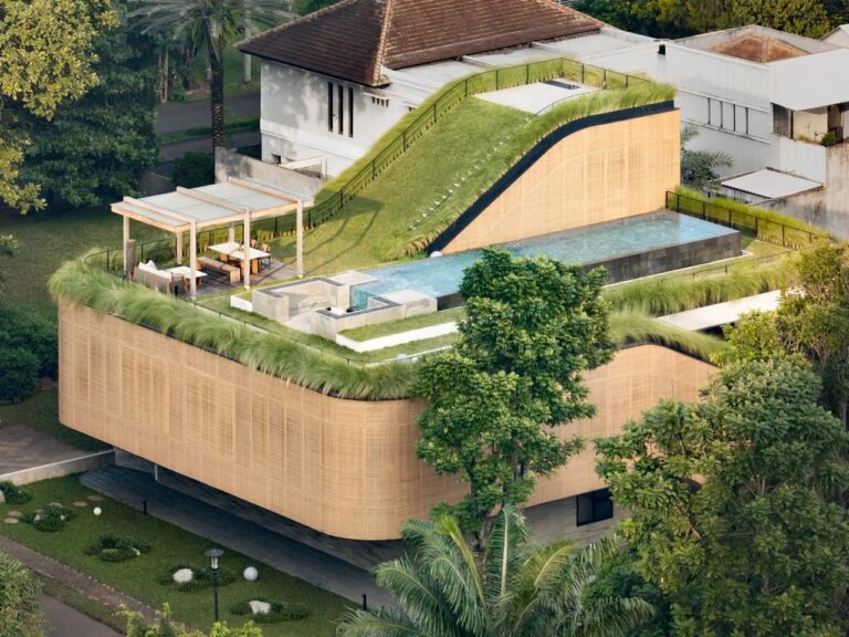 Aerial view of Split Mass Residence featuring a sloped green roof, swimming pool, wooden pergola, and woven synthetic rattan facade.