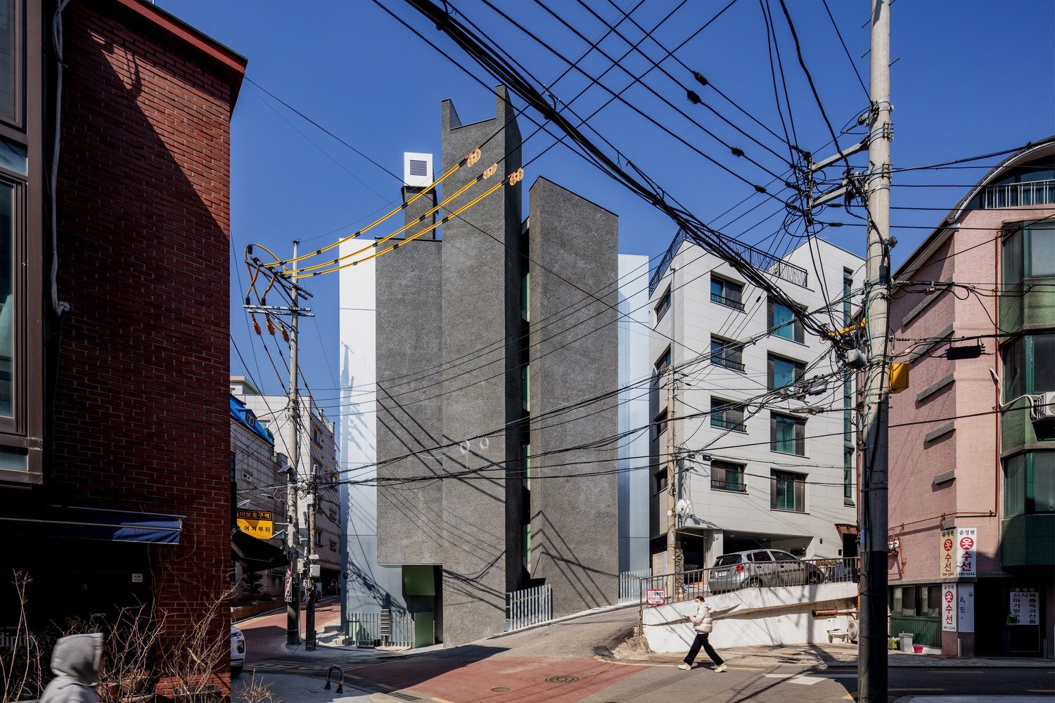Exterior front view of the Bangbae rental facility building showing the tall rough concrete southern core and metal facade on a sloped street.