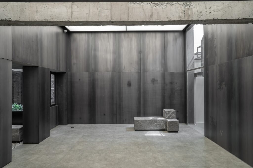 Spacious indoor room with stone benches under an overhead skylight framed by exposed concrete beams.
