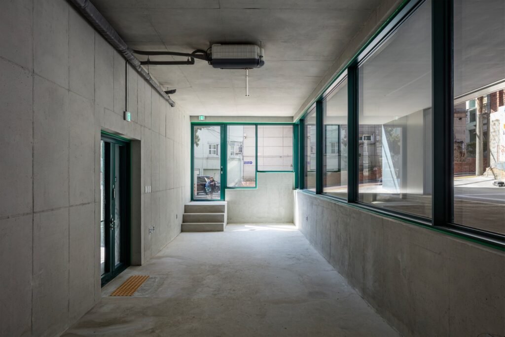 Empty interior rental unit space with exposed concrete walls, smooth ceiling, and green window frame.