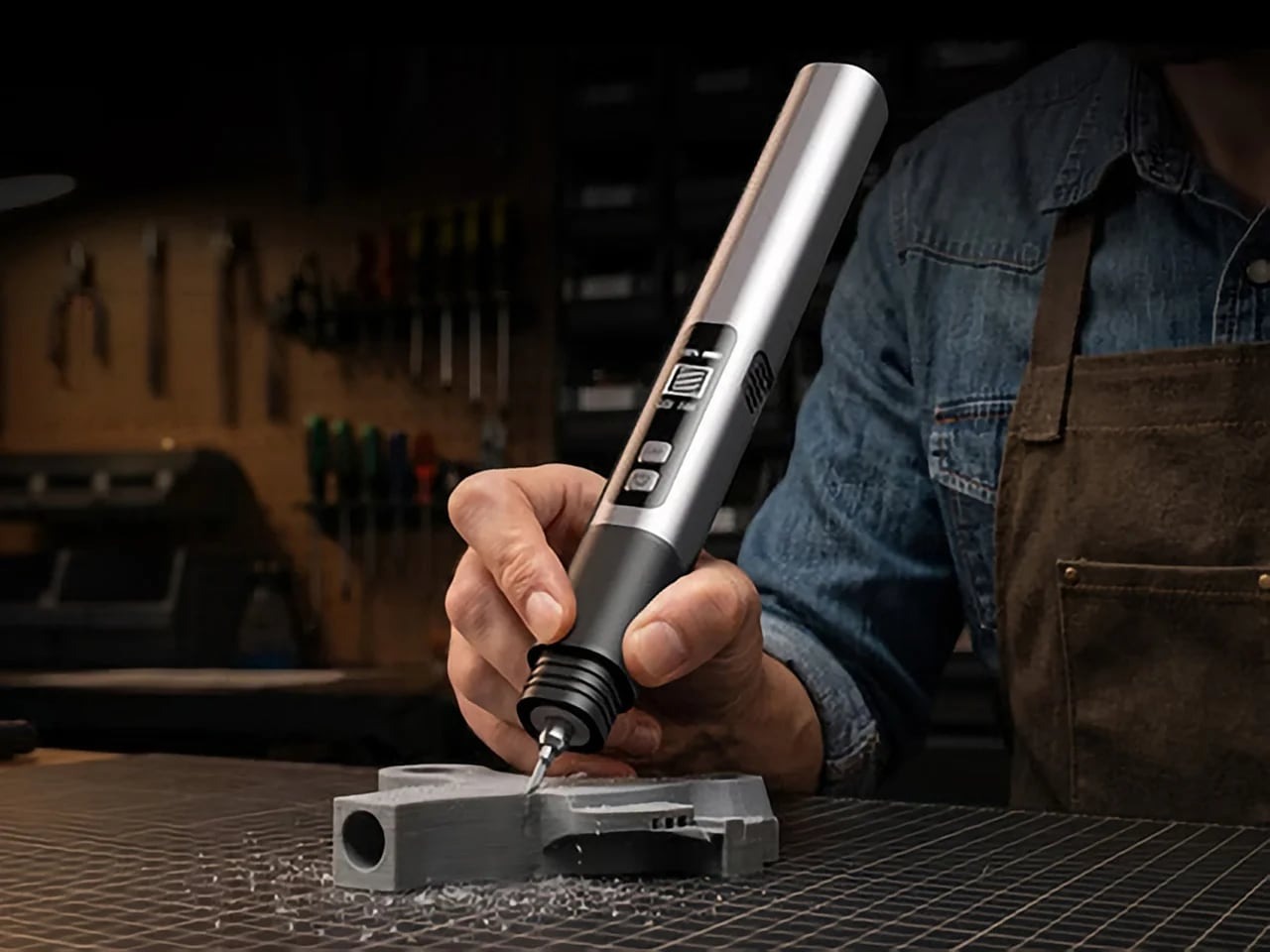 A close-up photograph of a user's hand holding the pen-like Sonic Cutter Max 10, demonstrating precise detailing on a 3D-printed grey plastic part with visible plastic shavings.