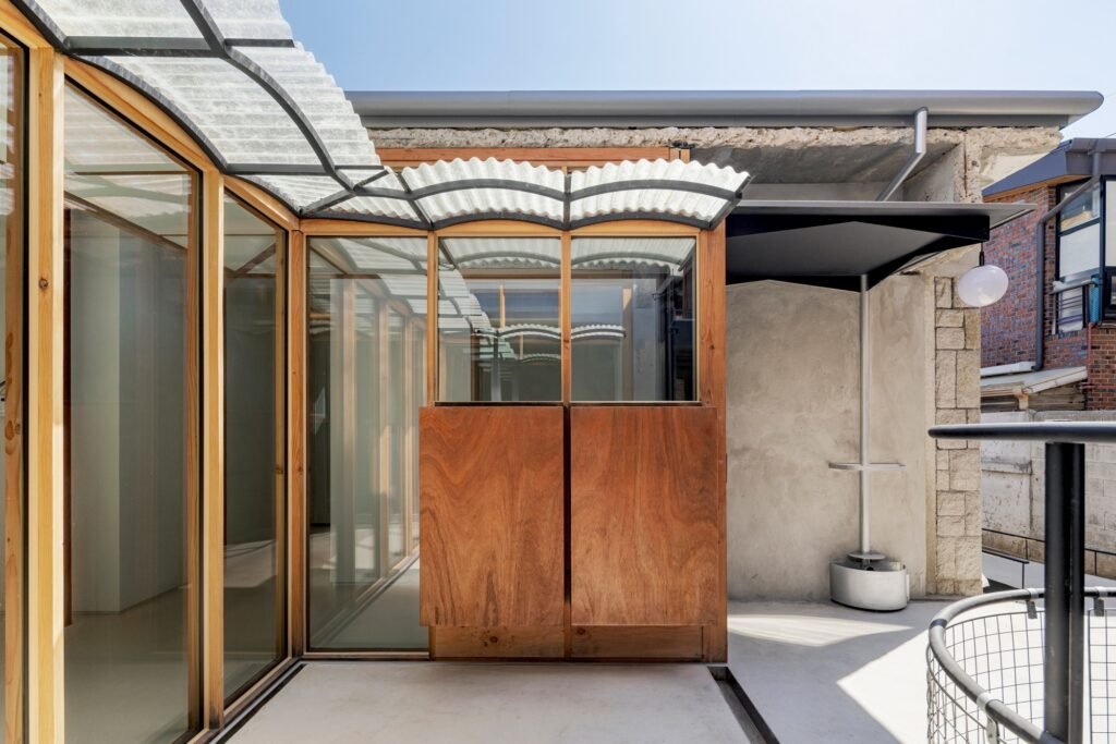 Close-up of the central courtyard at Saekdong House featuring timber frame glazing, a jade-green corrugated FRP eaves canopy, and exposed concrete ring beam.