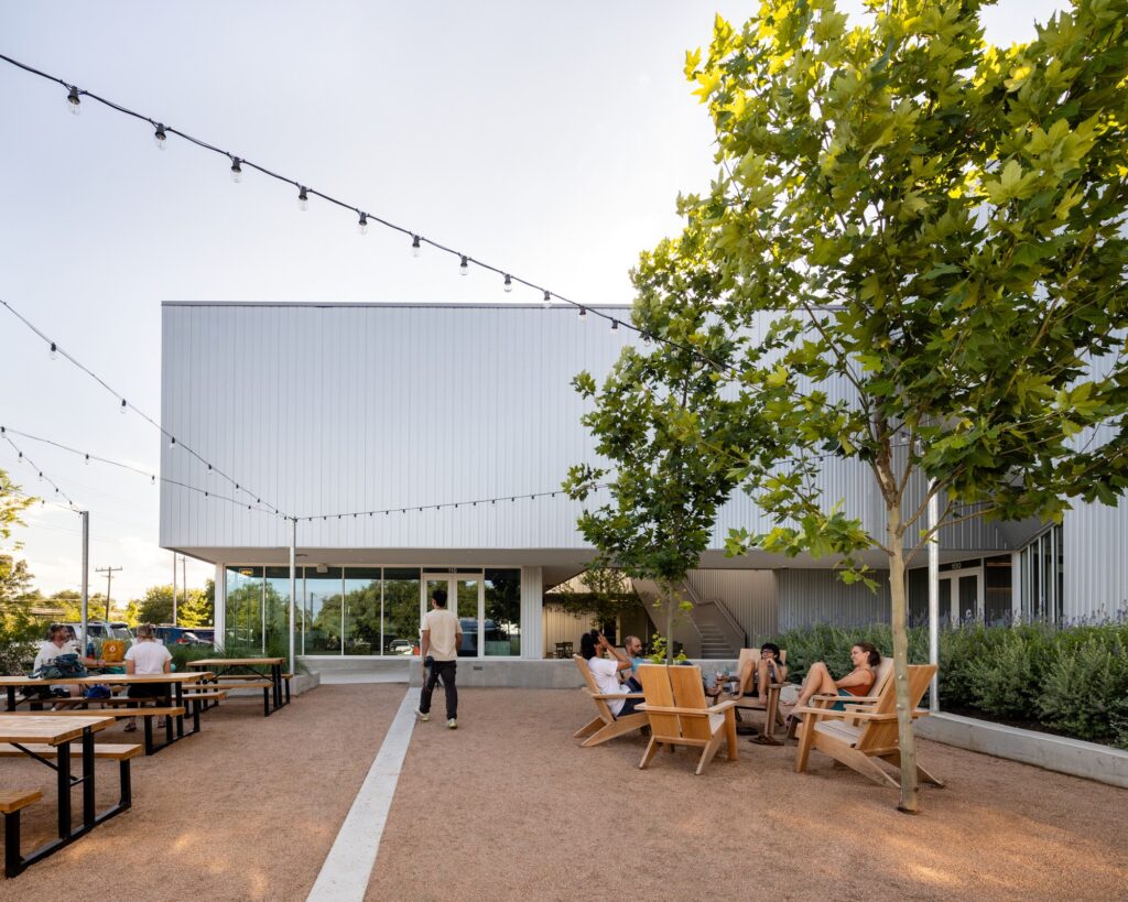 Outdoor seating court with string lights, wooden chairs, and picnic tables outside Crux South cafe entrance.