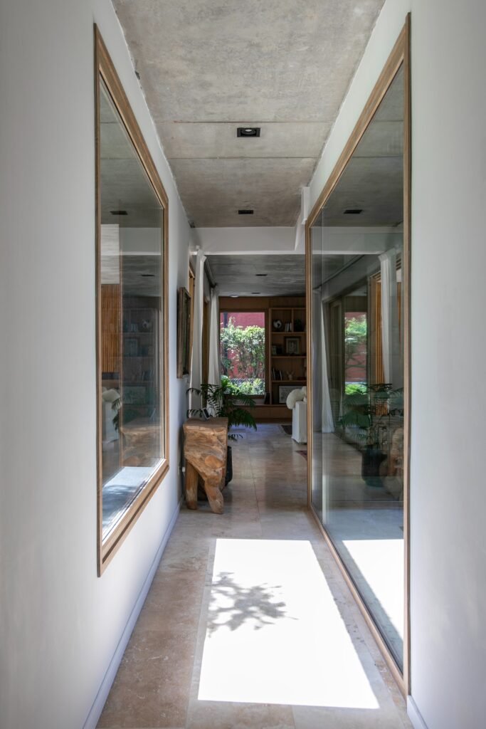 Bright hallway featuring full-height glass windows overlooking an outdoor space, concrete ceilings, and stone tile flooring.