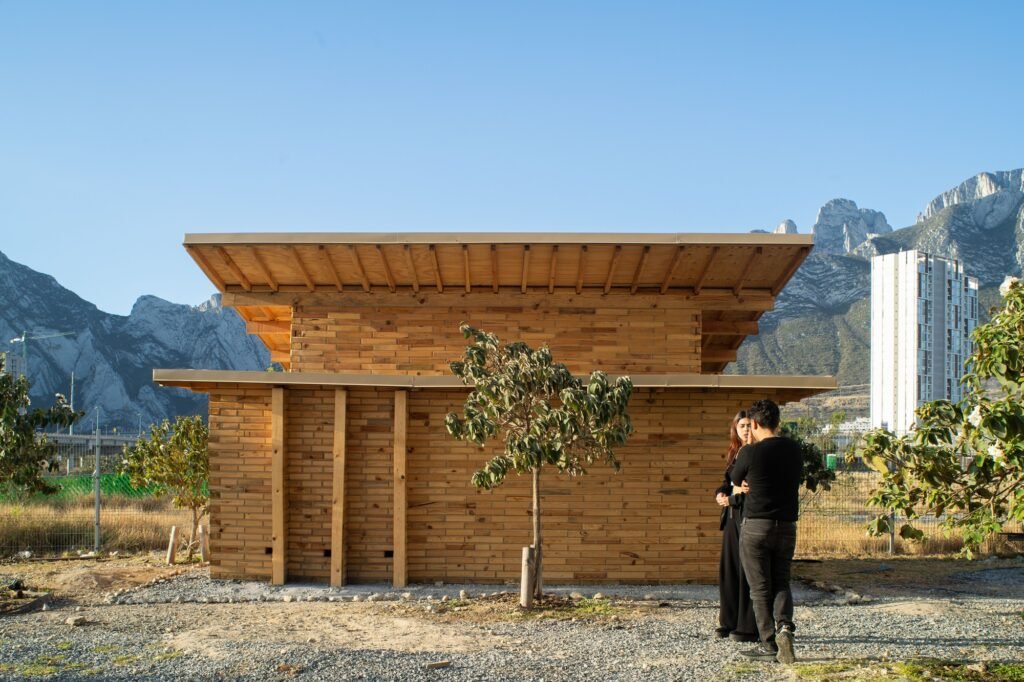 Visitors standing near the timber facade of La Grieta Pavilion with layered wooden blocks and a sloped roof structure.
