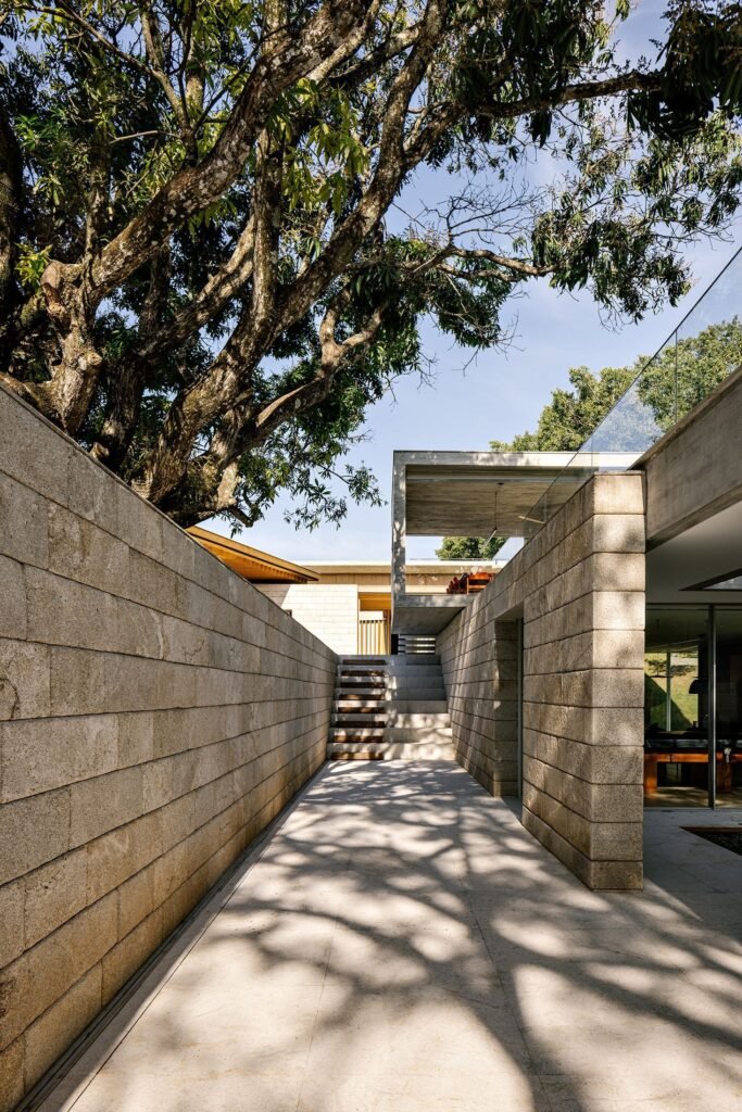 Triangular-section stone retaining wall and concrete pathway navigating the sloping terrain of Casa do Bosque.