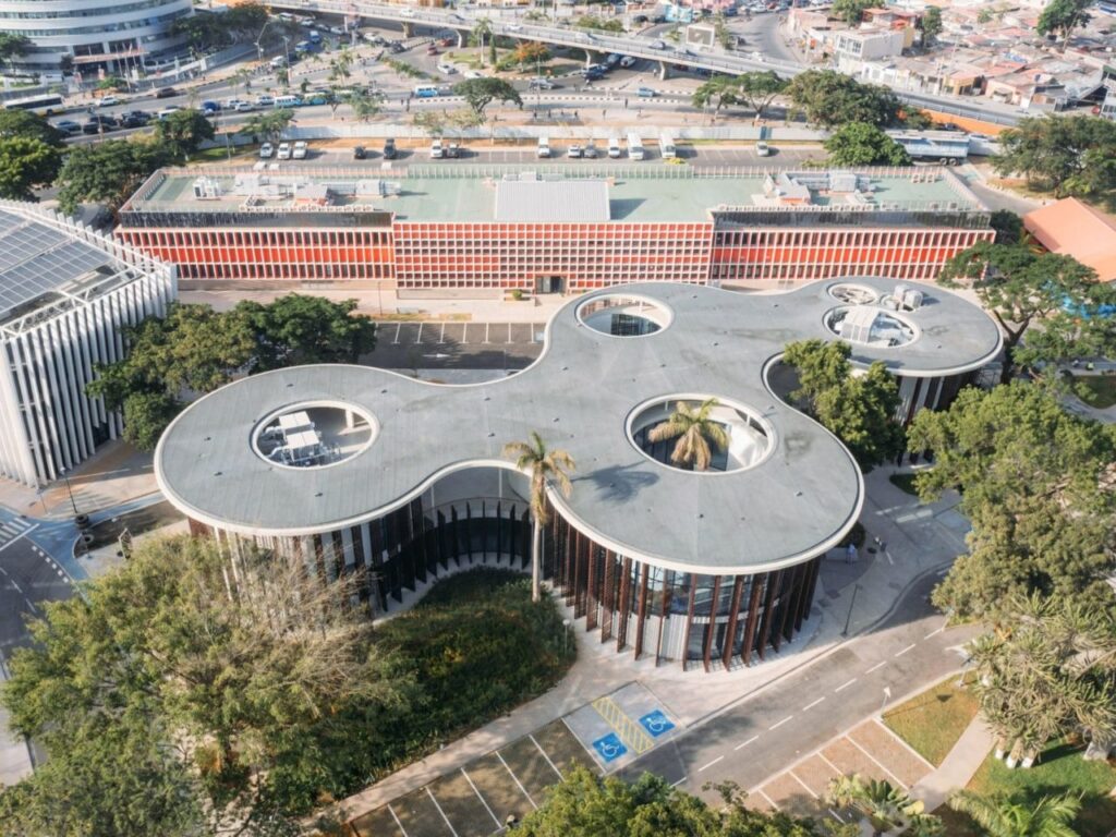 Aerial view of the curvilinear roof structure of Luanda Library featuring circular cutouts around existing mature trees.