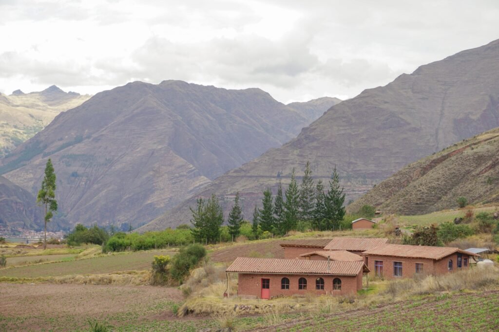 Exterior view of earthen adobe buildings of Kusca residence with clay tile roofs set on a hillside in the Sacred Valley near Cusco.