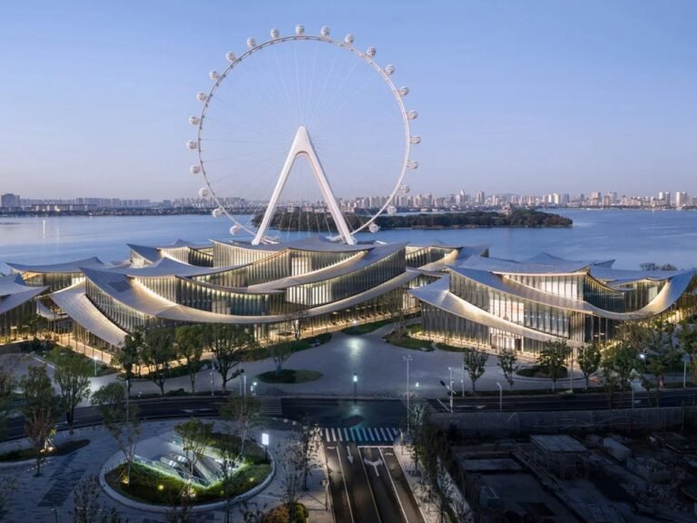 Front ground-level view of Suzhou Museum of Contemporary Art with ripple-like roofs framing a large Ferris wheel behind Jinji Lake.