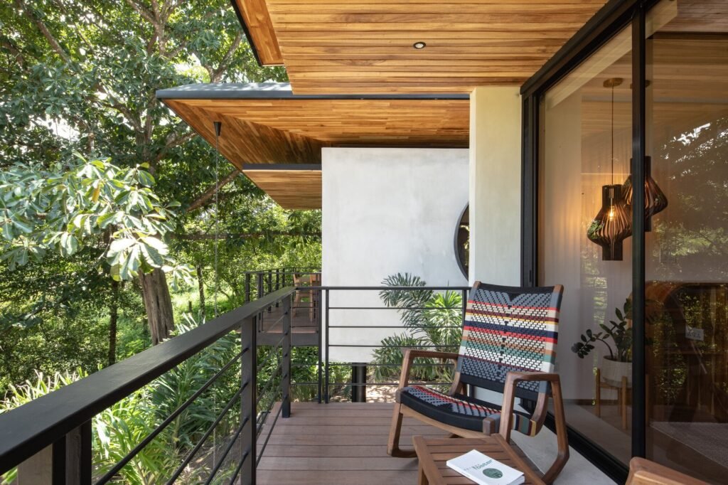 Covered balcony terrace with woven rocking chair, wooden soffit, and panoramic views of lush vegetation.