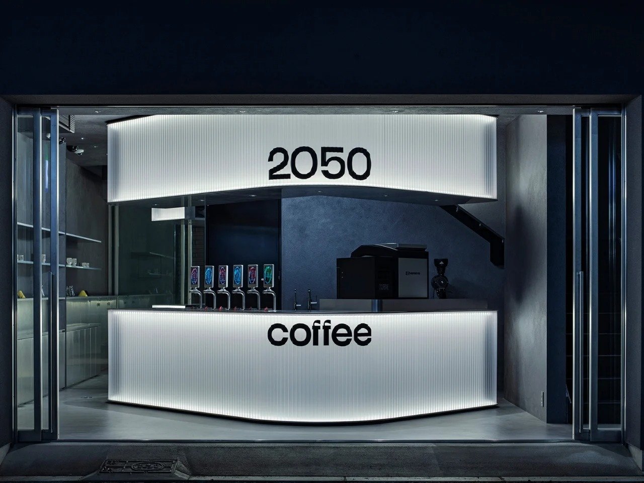Illuminated angled counter and header with 2050 Coffee logo at the storefront entrance in Osaka.